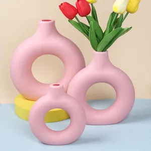 Macro view of three pink donut-shaped minimalist vases with colorful artificial tulips
