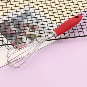 Dettaglio di una frusta manuale in acciaio inossidabile con manico ergonomico in silicone rosso.