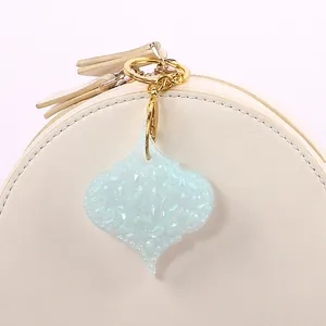 Close-up of a light blue glitter resin teardrop keychain charm on a beige bag