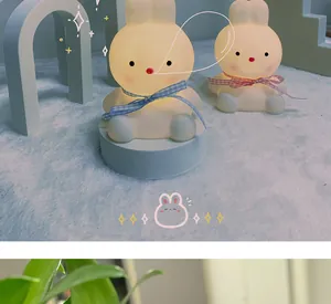 Detail view of two cute rabbit LED night lights with plaid bows on a plush white rug