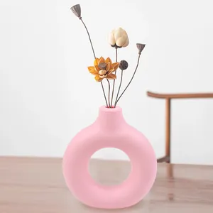Detail view of a pink doughnut-shaped vase with dried flower arrangement on a wooden table