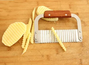 Close-up of wavy stainless steel blade cutting potato chips on a wooden board