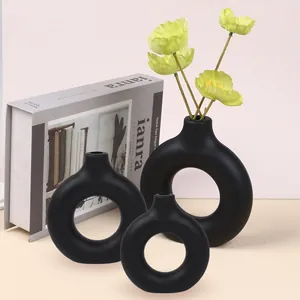 Detail view of three matte black donut vases with yellow flowers on neutral background