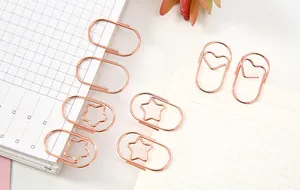 Nahaufnahme kreativer Büroklammern aus Roségold in Herz- und Sternform auf dem Papier
