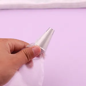 Close-up of hand holding a disposable PE piping bag with a stainless steel icing nozzle.