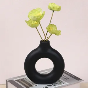 Close-up of a minimalist matte black donut-shaped vase with yellow flowers on a book.