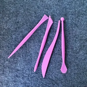 Dettaglio di quattro strumenti per modellare il fondente rosa su superficie grigia.