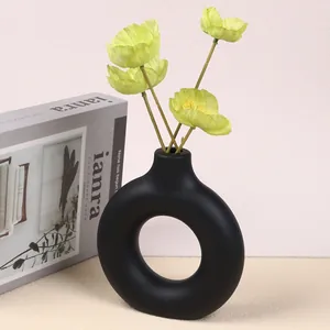 Modern matte black doughnut vase with green flowers on a minimalist office desk
