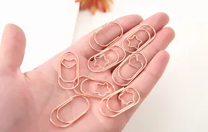 Detailansicht von roségoldenen Metall-Büroklammern in Herz- und Sternform, in der Hand gehalten