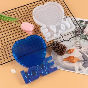 Dettaglio dello stampo in silicone LOVE a cuore e del pezzo in resina blu con glitter.