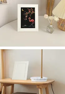 DIY white cardboard frame for A5 scratch art and photos displayed in a cozy room setting