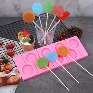 Molde redondo de silicona para piruletas con caramelos de colores sobre fondo gris