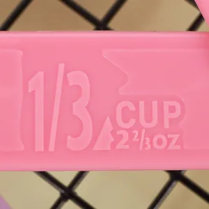 Macro detail of embossed 1/3 cup and 2 2/3 oz measurement on pink plastic spoon