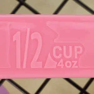 Macro detail of pink plastic measuring spoon showing embossed 1/2 cup 4 oz measurement scale