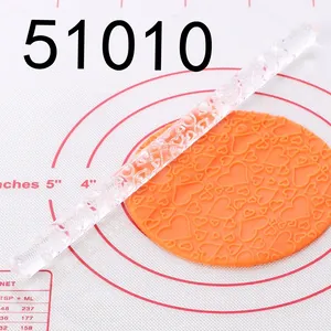 Close-up of transparent acrylic rolling pin embossing heart patterns on orange fondant