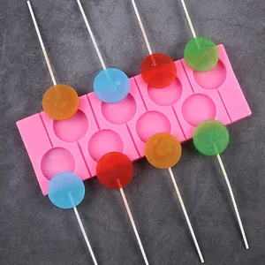 Molde de silicona rosa para piruletas redondas con caramelos de colores en fondo piedra