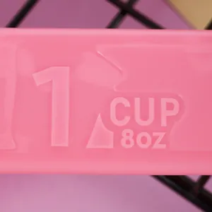 Close-up detail showing the molded 1 cup and 8oz markings on a pink plastic measuring spoon