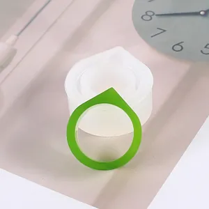 Détail du moule à bague en silicone translucide avec bague finie en résine verte brillante.