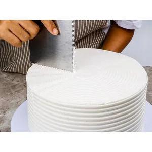 Detail view of a metal cake scraper creating precise textured patterns on white icing