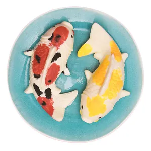 Vue détaillée de deux figurines réalistes de carpes koi en pâte à sucre sur une assiette bleue