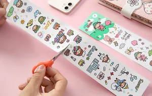 Close-up of cutting cartoon DIY journal stickers with scissors on pink background