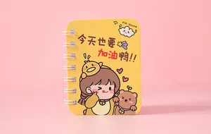 Macro view of a mini yellow spiral notebook featuring cute cartoon girl and bear characters.