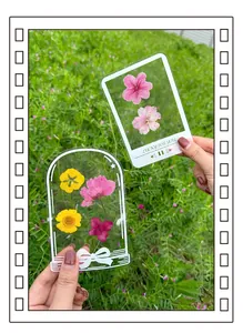 Hand holding transparent DIY pressed flower bookmarks in a natural green meadow.
