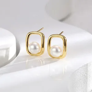Detalle de pendientes minimalistas de perlas con marco rectangular dorado para mujer