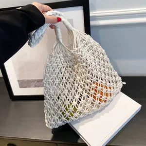 Bolso de playa de macramé blanco sostenido a mano con frutas frescas para verano