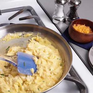 Close-up detail shot of a heat resistant blue silicone spatula stirring fluffy scrambled eggs.