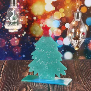 Handmade green Christmas tree resin ornament on a rustic wooden table with festive bokeh lights.