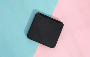 Detail of closed black portable square makeup mirror on pink and blue background