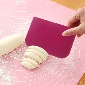 Purple plastic dough scraper being used to cut dough on a pink silicone baking mat