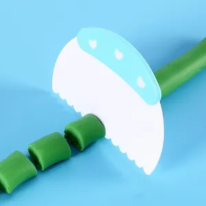 Primer plano de un raspador de masa cortando arcilla verde sobre un fondo azul suave