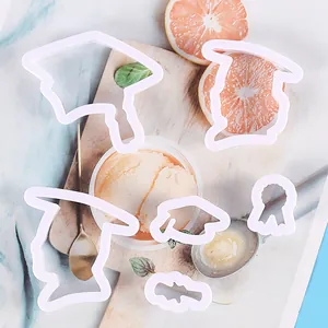 Set witte plastic koekjesuitstekers met afstudeerthema gepresenteerd op houten plank.
