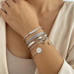 Primer plano de brazaletes de plata minimalistas con diseños de nudos y giros en la muñeca.