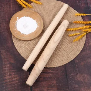 Primer plano de rodillos de madera de haya sobre un tapete con harina y espigas de trigo.