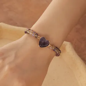 Primer plano detallado de una pulsera tejida a mano con piedra de corazón púrpura y cuentas.