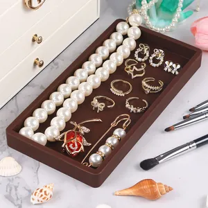 Brown silicone tray organizing various jewelry like pearl necklaces and gold rings