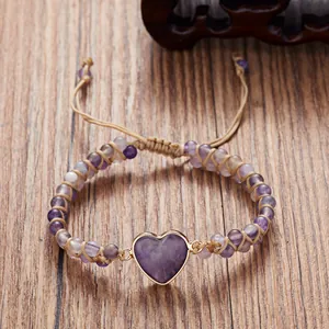 Detalle de una pulsera de cuentas de piedra púrpura tejida a mano con corazón dorado.
