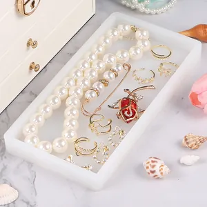 Macro view of a white silicone jewelry storage tray with pearl necklace and rings