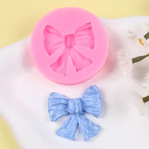 Detalle del molde de silicona rosa para lazo y un lazo de fondant azul terminado.
