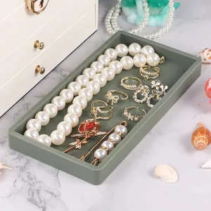 Dark green silicone jewelry tray organizer with pearl accessories on marble surface