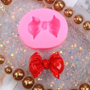 Vista detallada de un molde de silicona para lazos rosa y un lazo de fondant rojo
