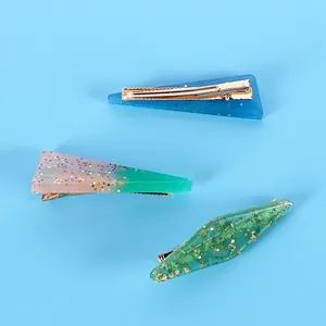 Détail de trois barrettes en résine pailletée aux tons bleu, vert dégradé et rose pastel.