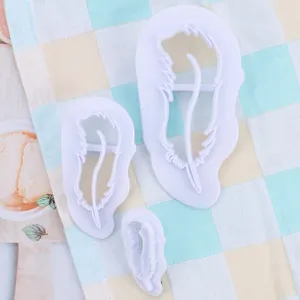 Detailopname van drie witte plastic fondant-uitstekers in veervorm op een geruite doek