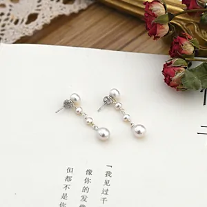 Close-up detail of elegant white freshwater pearl drop earrings on a minimalist card