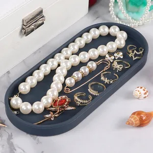 Close-up of a charcoal grey oval silicone storage tray organizing jewelry and rings