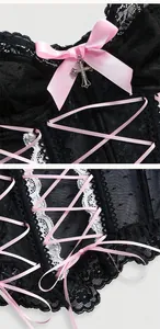 Dettaglio di un corsetto in pizzo nero con fiocco rosa e ciondolo a forma di croce.
