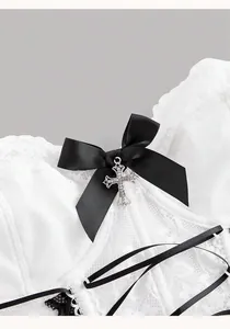 Dettaglio di corsetto in pizzo bianco con fiocco nero e ciondolo a croce